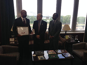 Three men talking to each other. One man is holding a Badge of Bravery award plaque.