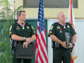 Two men wearing officer uniforms and holding Badge of Bravery plaques at the award ceremony.