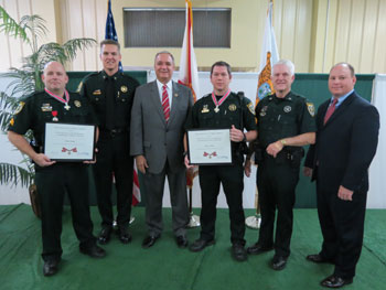 A group of people standing together in a row at the Badge of Bravery awards ceremony. Some are holding awards.