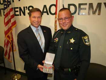 Two people smiling at the camera and holding a Badge of Bravery award