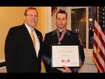 Two people together at the Badge of Bravery award ceremony. One man is holding an award plaque.
