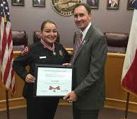 Two people standing together at the Badge of Bravery awards ceremony, holding an award plaque, and smiling at the camera
