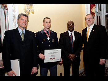 A group of people standing together in a row at the Badge of Bravery awards ceremony. One man is holding an award plaque.