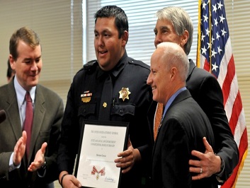 A group of people standing together in a row at the Badge of Bravery awards ceremony. One man is holding a Badge of Bravery award plaque.