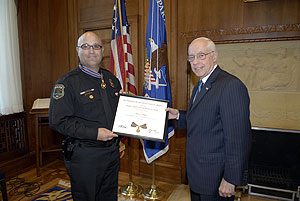 two men standing in a room, smiling at the camera, and holding a Medal of Valor award plaque between them