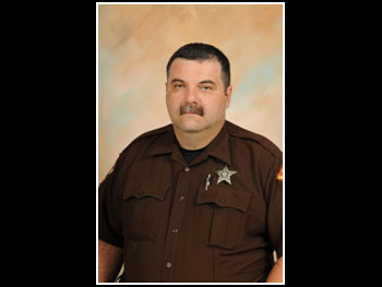 a head and shoulders portrait of a man in a sheriff's uniform against a neutral background facing the camera