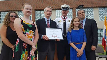 A group of people standing together. The man in the middle is holding a Badge of Bravery award.