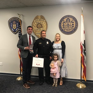 A group of people standing together. The man in the middle is holding a Badge of Bravery award.