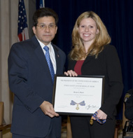 A man and woman standing on a stage and smiling at the camera. They are holding a Medal of Valor award plaque between them.