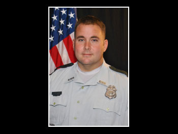 a head and shoulders portrait of a man in an officer's uniform facing the camera and standing in front of an American flag