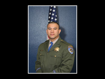 a portrait of a man in a sheriff uniform standing in front of an American flag and facing the camera
