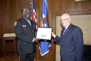 two men standing in a room, smiling at the camera, and holding a Medal of Valor award plaque between them
