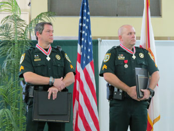 Two men wearing officer uniforms and holding Badge of Bravery plaques at the award ceremony.