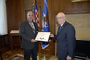 two men standing in a room, smiling at the camera, and holding a Medal of Valor award plaque between them