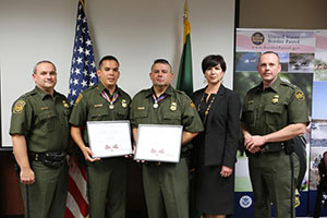 A group of people standing together in a row at the Badge of Bravery awards ceremony. Some are holding award plaques.