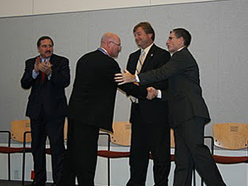 A group of four people. Two of them are shaking hands with each other.
