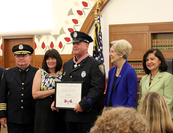 A group of people standing together. The man in the middle is holding a Badge of Bravery award.