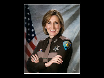 a head and shoulders portrait of a woman in an officer's uniform smiling at the camera and standing in front of an American flag 