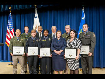 A group of Medal of Valor award recipients standing together on a stage, holding award plaques, and wearing officer uniforms
