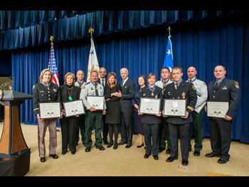 A group of Medal of Valor award recipients standing together on a stage, holding their award plaques, and wearing their officer uniforms.