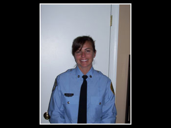 a photo from the waist up of a dark-haired woman firefighter wearing a blue dress shirt and dark tie smiling at the camera
