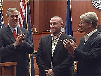 two men applauding as another man receives the Badge of Bravery award