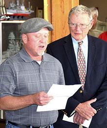  A man reading aloud from a piece of paper. Another man is standing nearby.