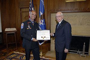 two men standing in a room, smiling at the camera, and holding a Medal of Valor award plaque between them